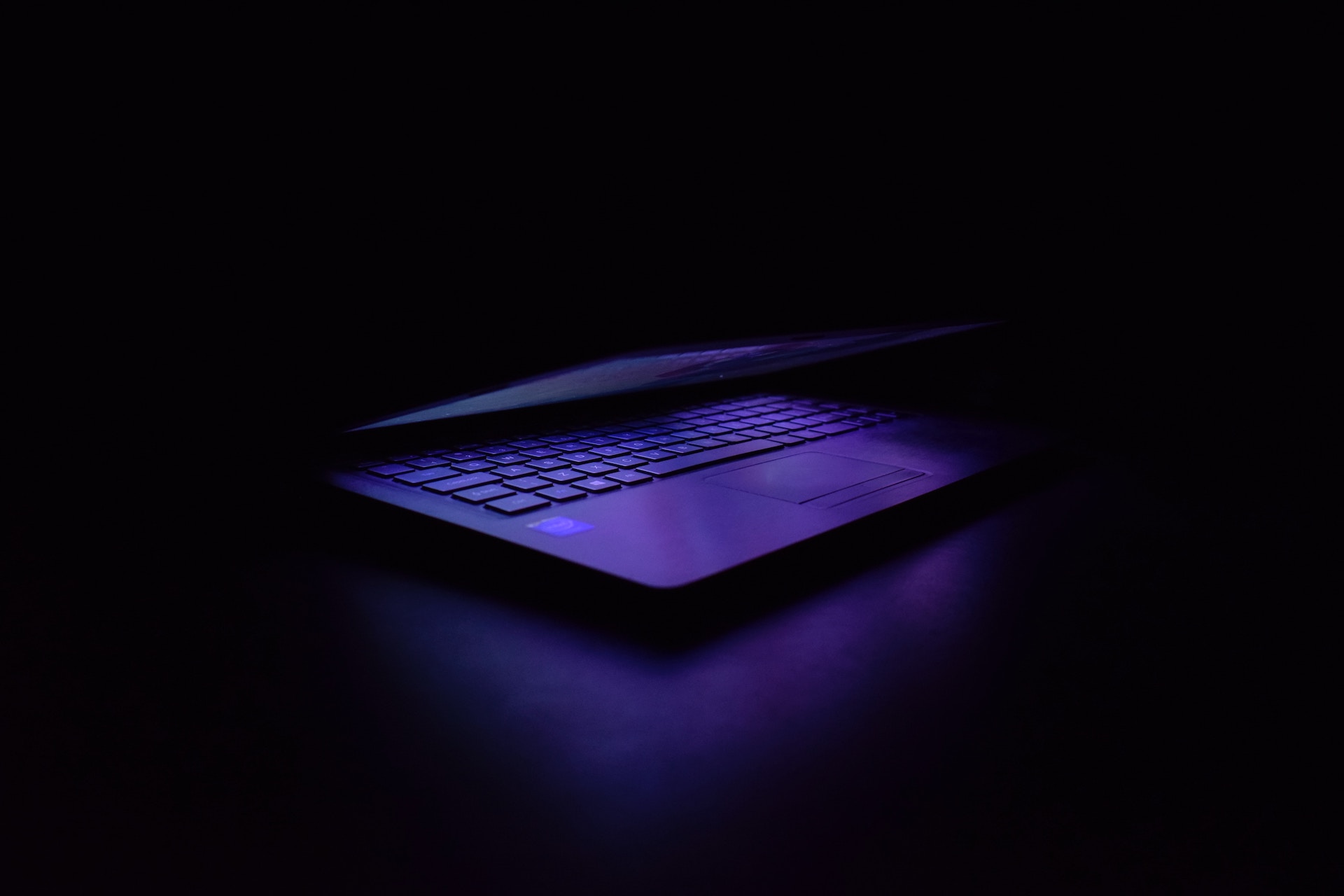 laptop half closed with purple light shining against a dark black background