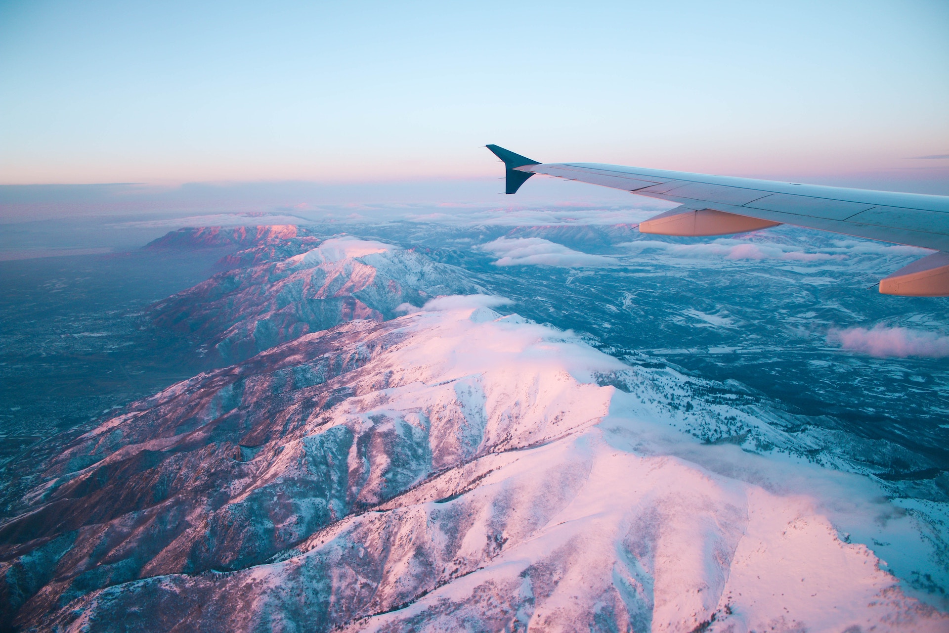 shot of a wing of an aeroplane flying over snow covered mountains